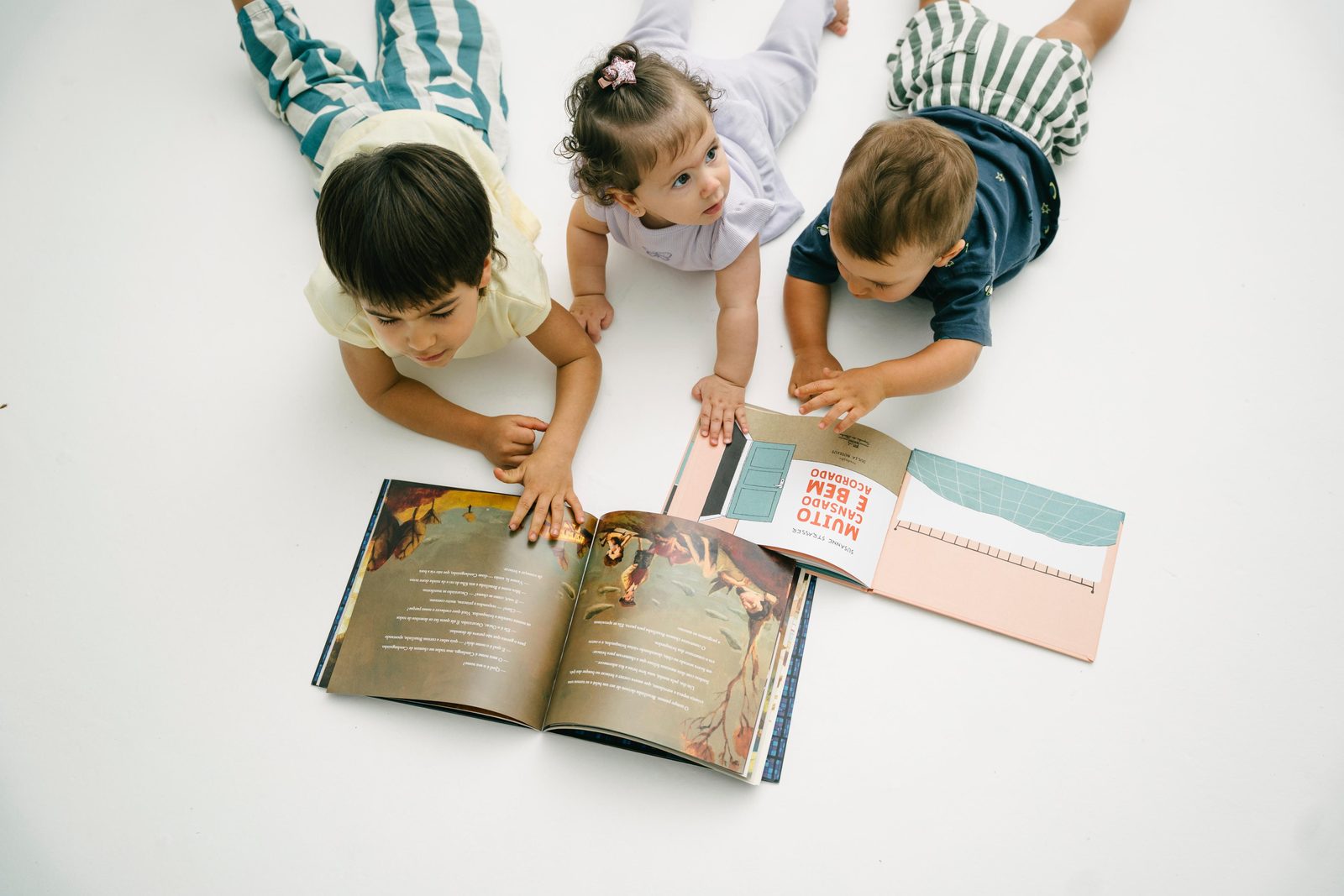 Três crianças pequenas — um bebê e dois meninos — lendo livros ilustrados juntas no chão